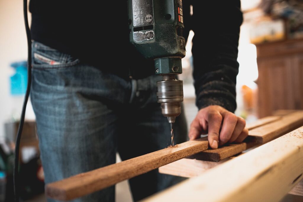 pexels-photo-1094767 Close-up of a person using an electric drill on a wooden plank, showcasing detailed woodworking skills.